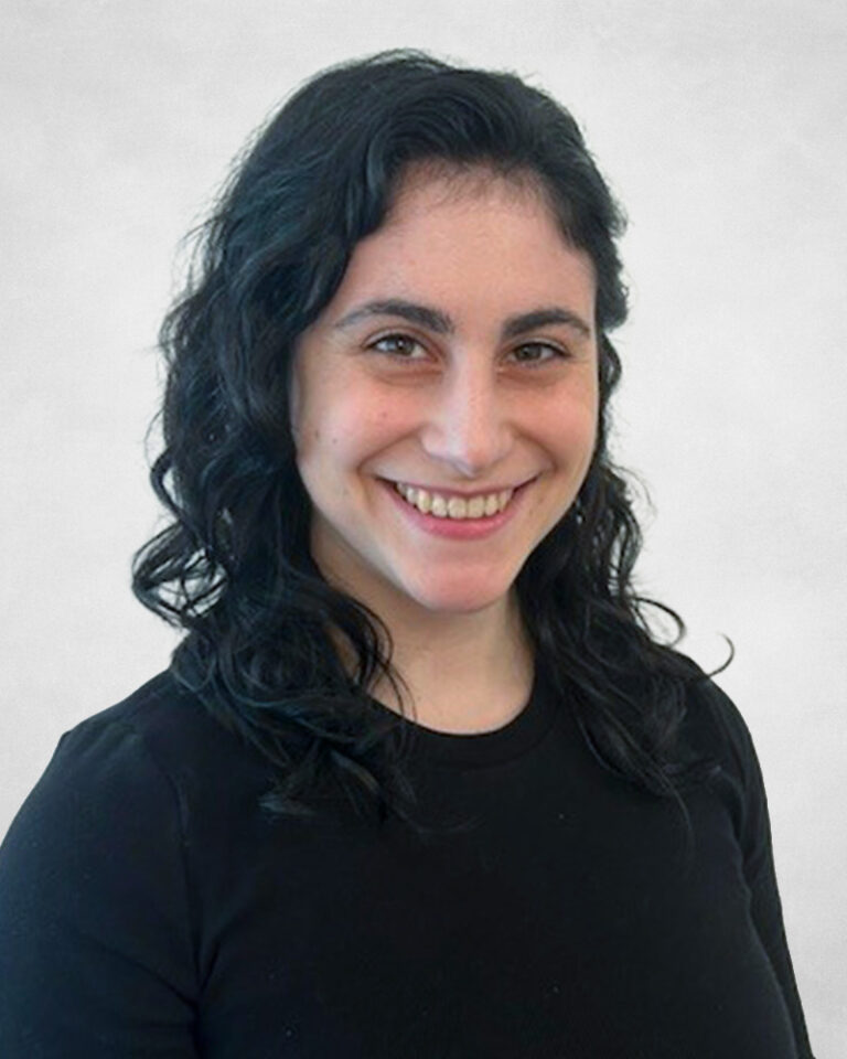 Daniela Luongo, A woman with wavy dark hair wearing a black top smiles at the camera against a plain, light grey background.