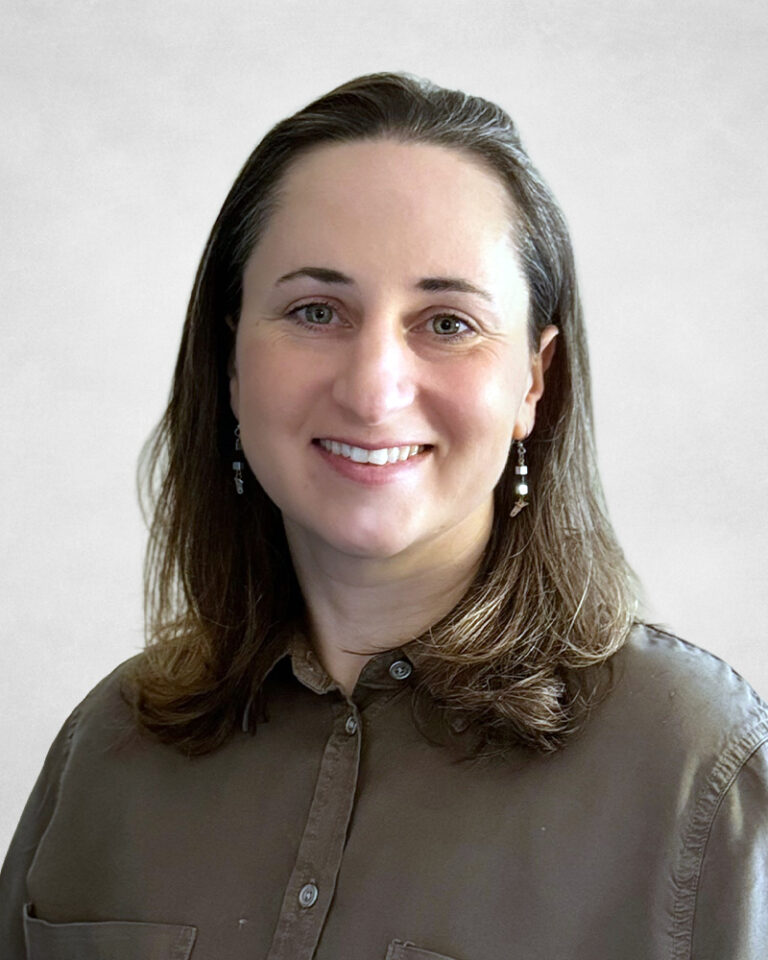 Esther Rottenstreich has straight, shoulder-length brown hair. They are wearing a brown button-up shirt and dangling earrings.