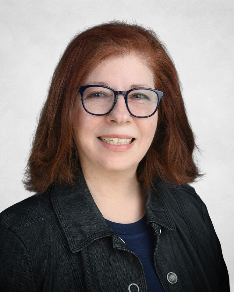 Fara Lambing has shoulder-length reddish-brown hair. She is wearing glasses, a dark jacket, and a navy blue shirt.