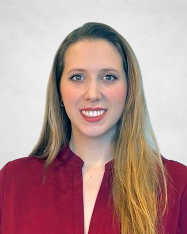 Julianna De Souza, A woman with long, straight blonde hair wearing a burgundy blouse smiles at the camera against a plain light grey background.