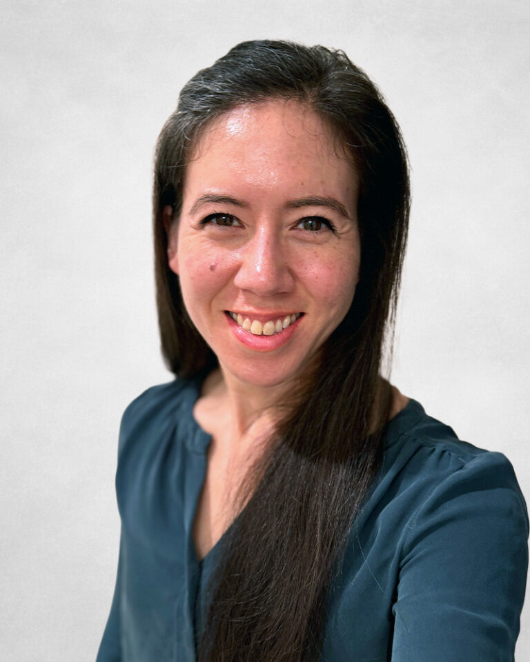 Natasha Chow, A woman with long dark hair and a dark blue blouse smiles at the camera against a plain light background.