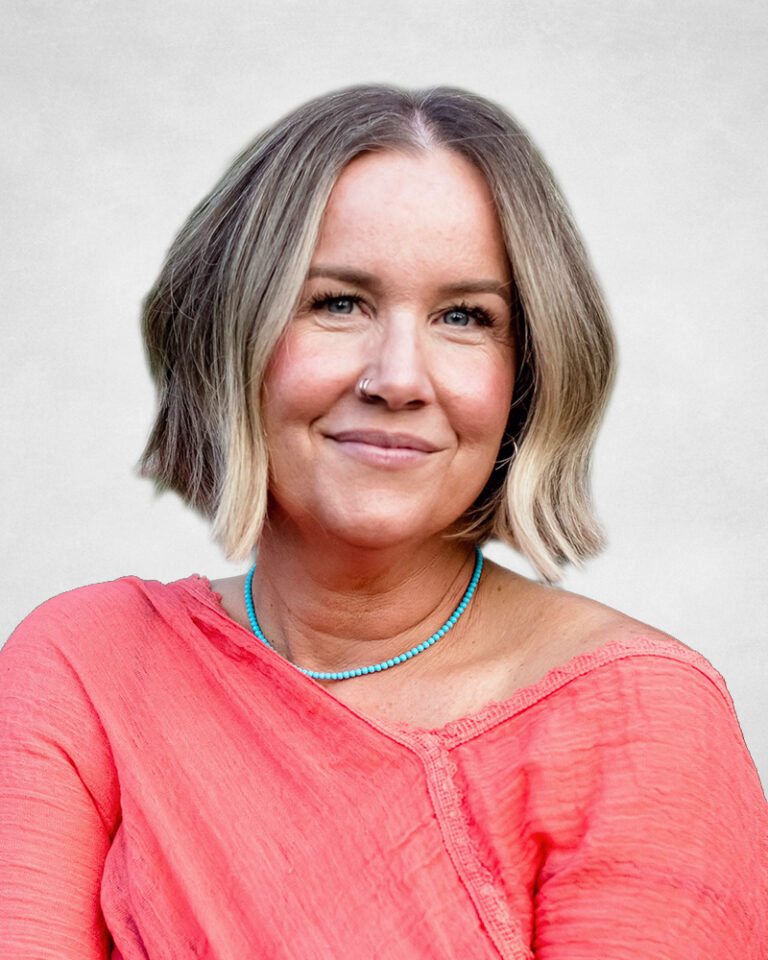 Shannon Rockall is a woman with a short, blonde bob haircut and a nose ring smiles softly. She is wearing a coral-coloured top and a turquoise beaded necklace.